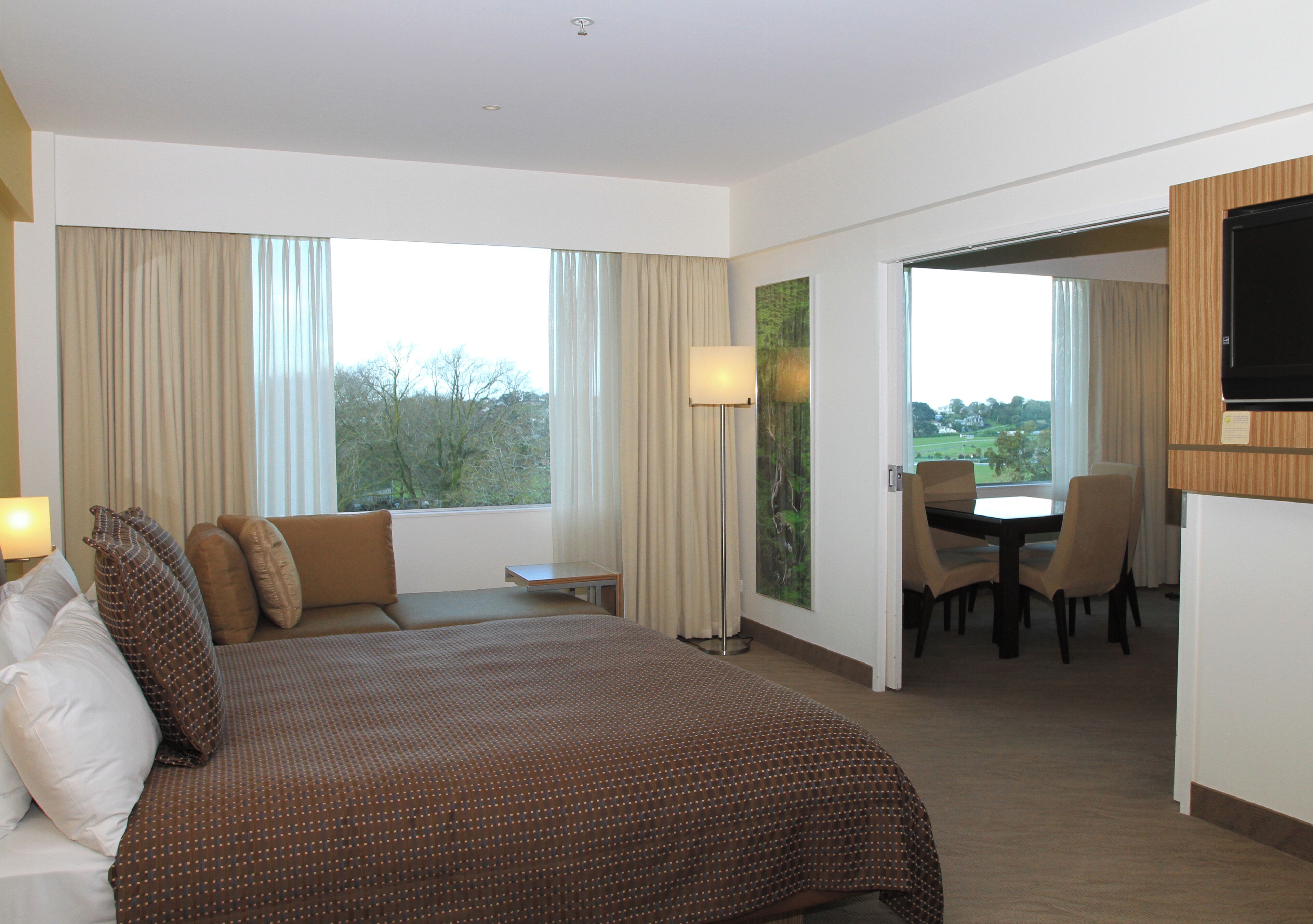 A hotel room with a large bed, a dining area, and a TV.