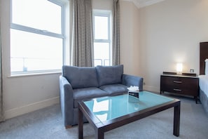 A hotel room with a grey sofa, a glass-top coffee table, a wooden nightstand, and a bed. - Bournemouth East Cliff by Belvilla (Bournemouth)