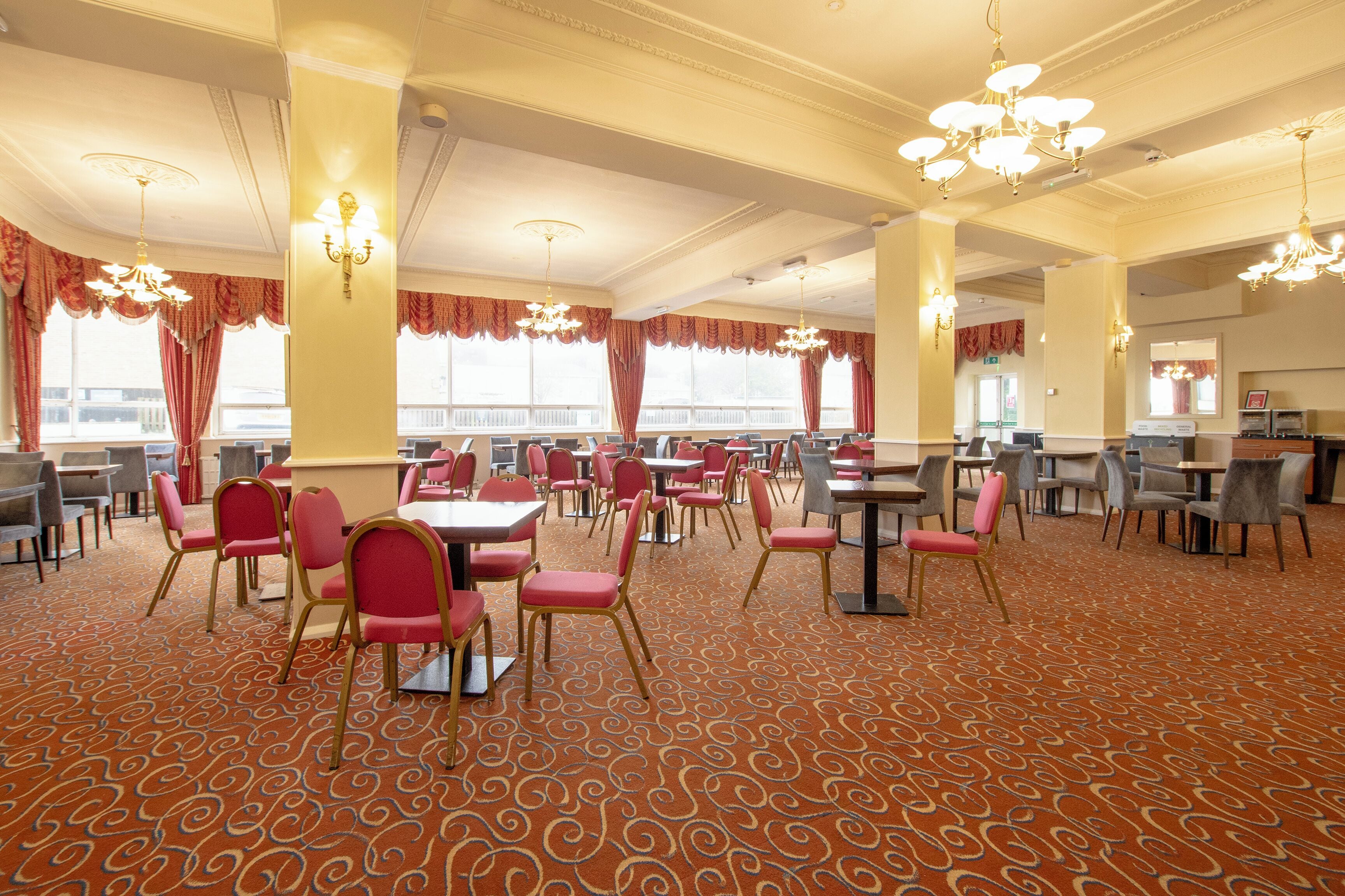 A spacious dining area with multiple tables and chairs, large windows, and ornate chandeliers.