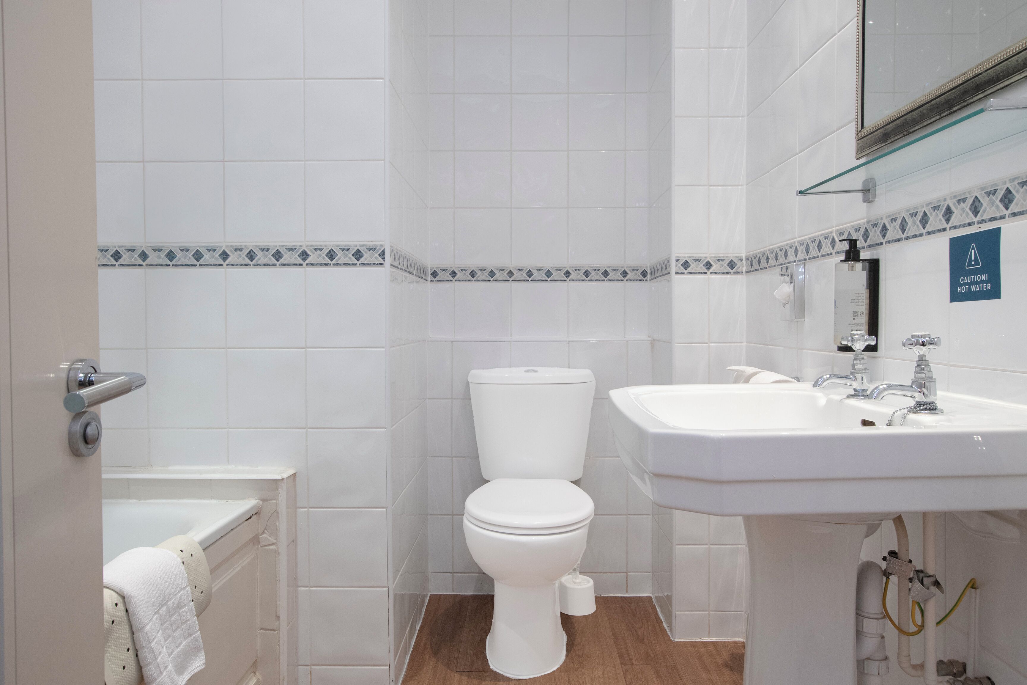 A bathroom with a toilet, sink, and a caution sign for hot water.