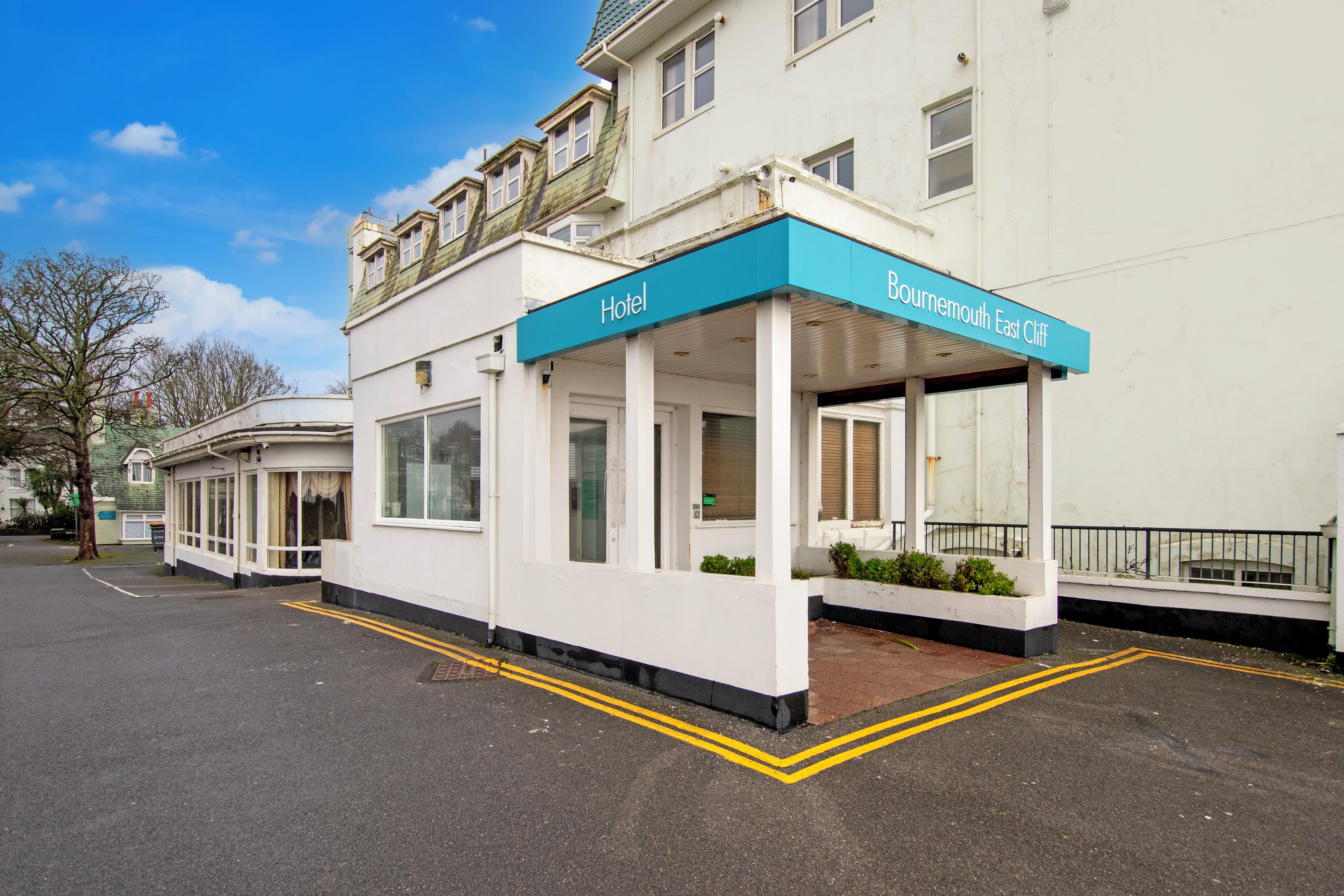 A hotel with a covered entrance, a sign reading 'Bournemouth East Cliff,' and a clear sky.