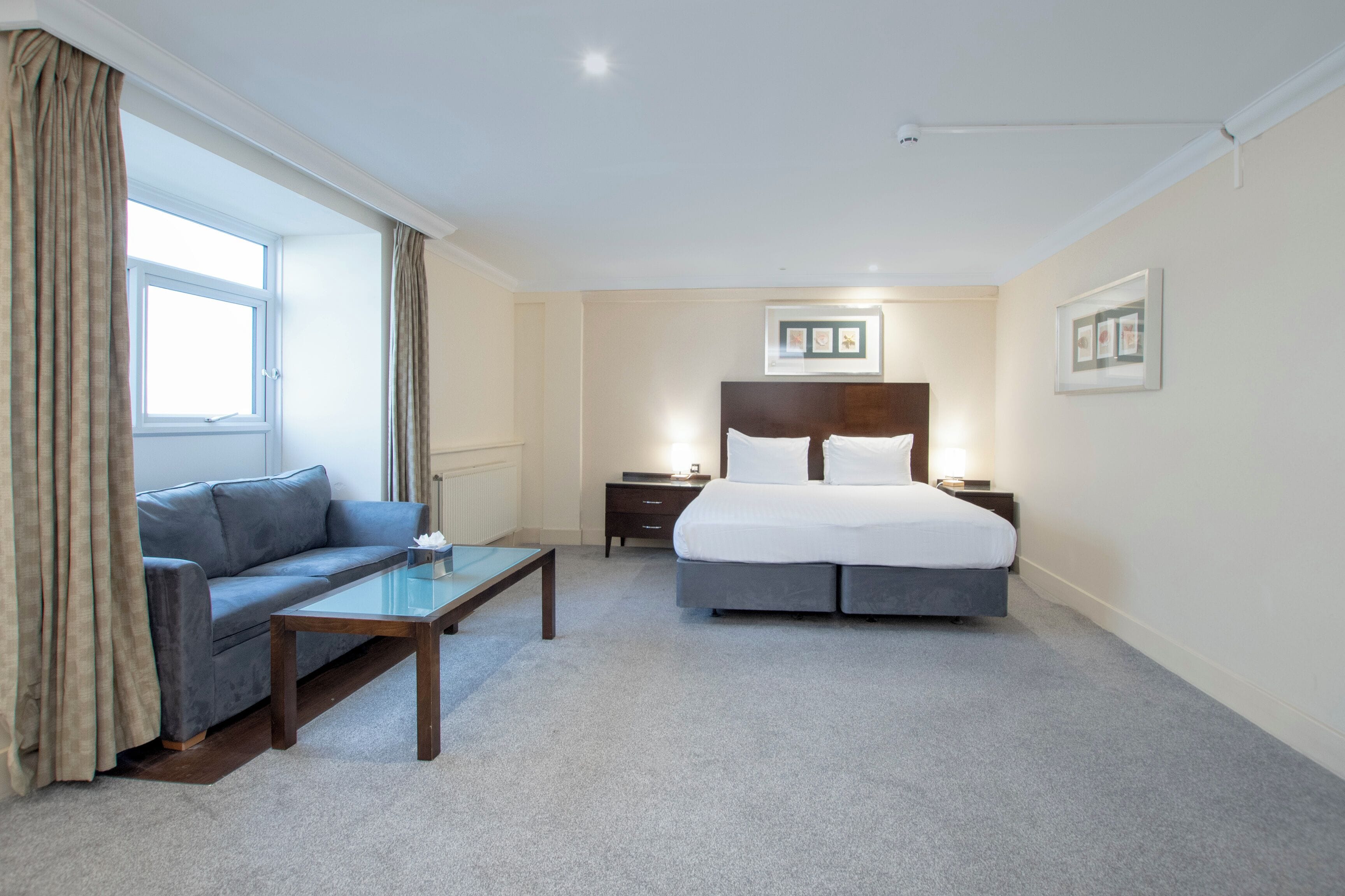 Une chambre d’hôtel avec un lit, un canapé, une table de chevet, une lampe et une fenêtre avec des rideaux.