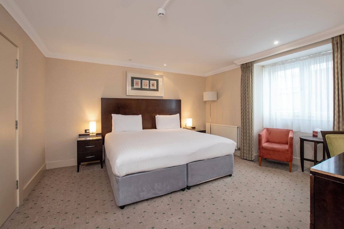 Une chambre d’hôtel avec un grand lit, une table de chevet, une lampe, une chaise et un bureau.