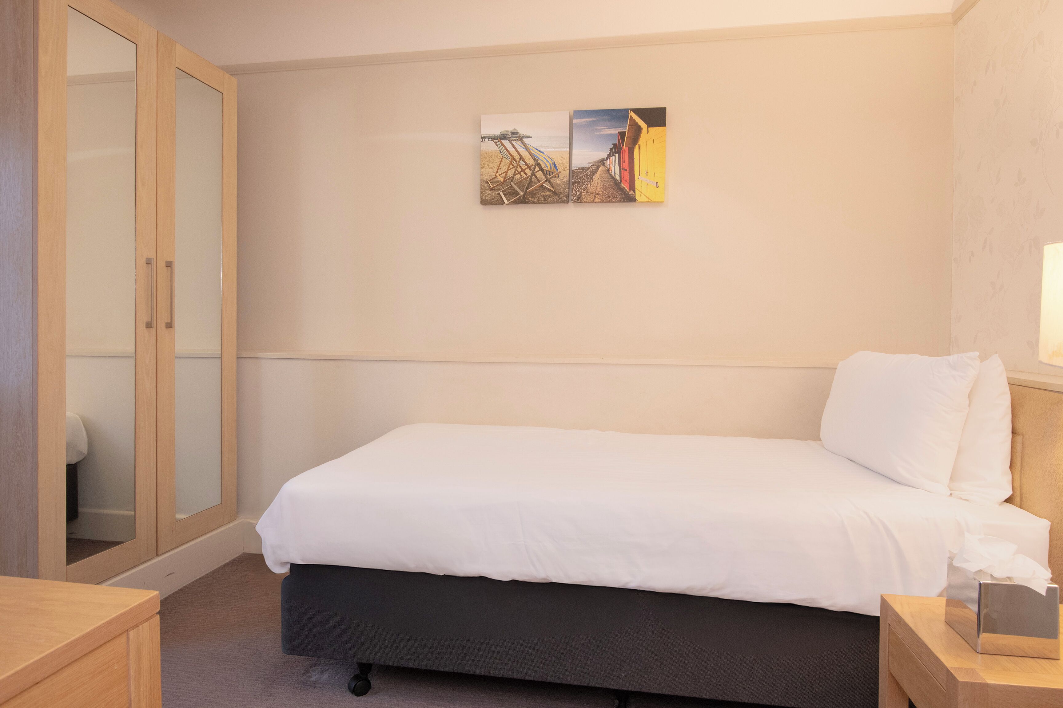A bedroom with a bed, a wooden wardrobe, and a wall-mounted painting.