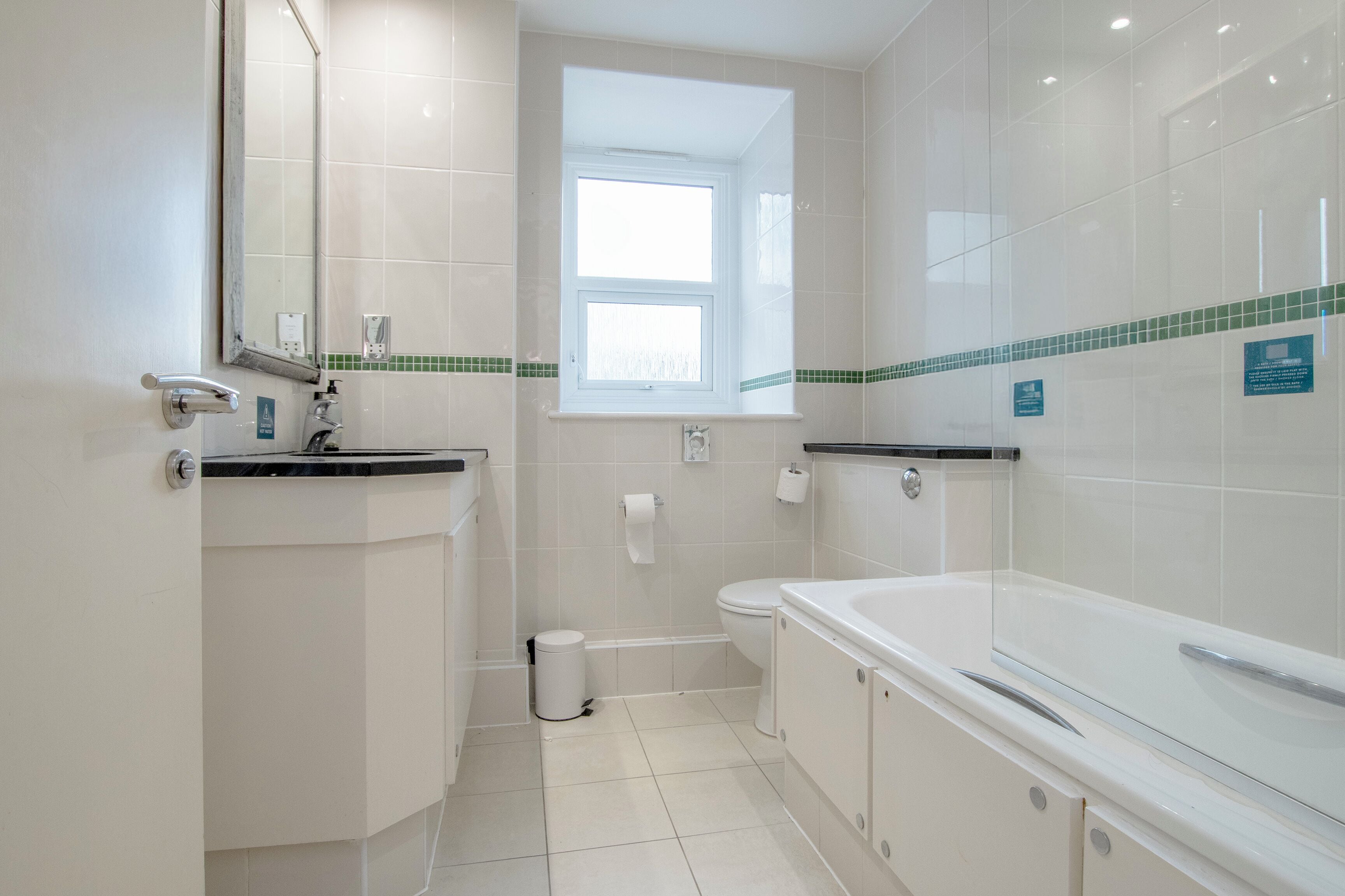 A bathroom with a toilet, sink, and bathtub, a window, and a trash can.