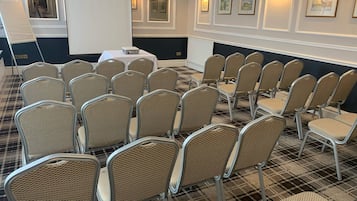 Un salón de conferencias con filas de sillas de mimbre, una pizarra y un proyector.