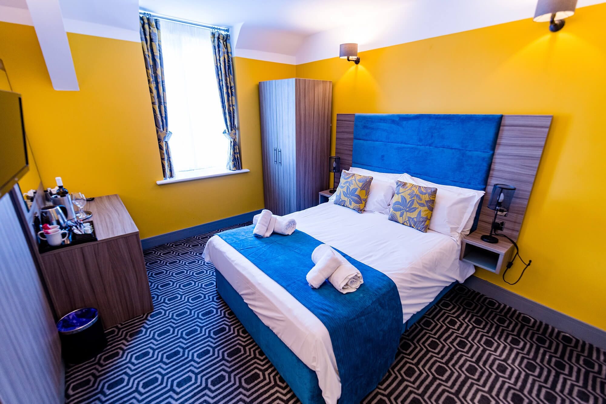 Habitación de hotel con una cama grande, una mesita de noche, un armario y una ventana con cortinas.