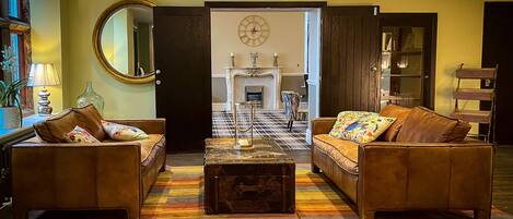 A living room with two leather sofas, a coffee table, and a colorful striped rug. There is a fireplace in the background, and the room has a large mirror on the wall.