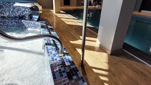 Un área de piscina con suelo de baldosas, baranda de metal y piso de madera.