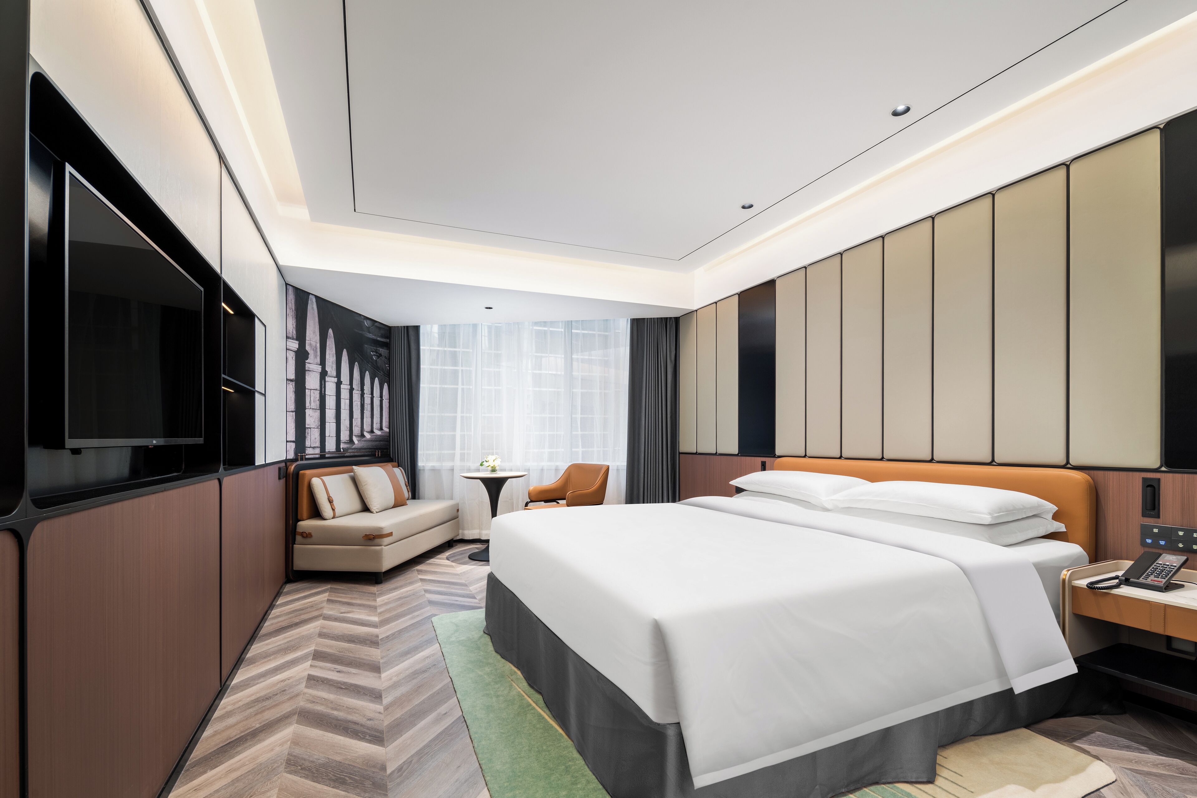 A modern hotel room with a large bed, a TV, a sofa, and a desk.