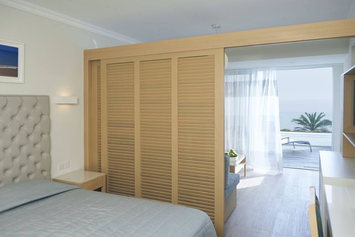 Une chambre avec un lit, une table de chevet, une armoire en bois et un balcon avec vue.