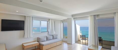 Una habitació d'hotel moderna amb un llit gran, un sofà, una taula de treball i un balcó amb vista a l'oceà.