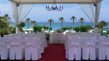 An outdoor wedding setup with a red carpet, white chairs with bows, and a view of the ocean.