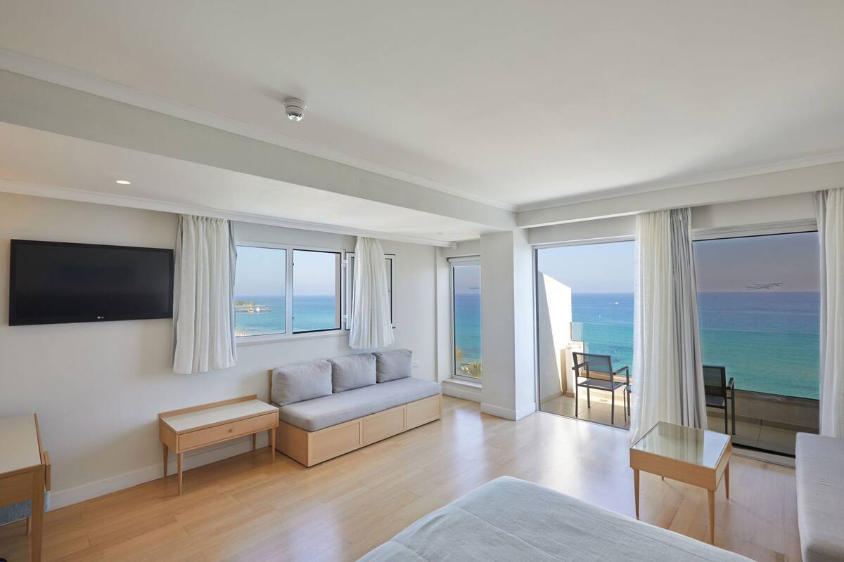 Une chambre d’hôtel moderne dotée d’un grand lit, d’un canapé, d’une télévision et d’un balcon offrant une vue sur l’océan.