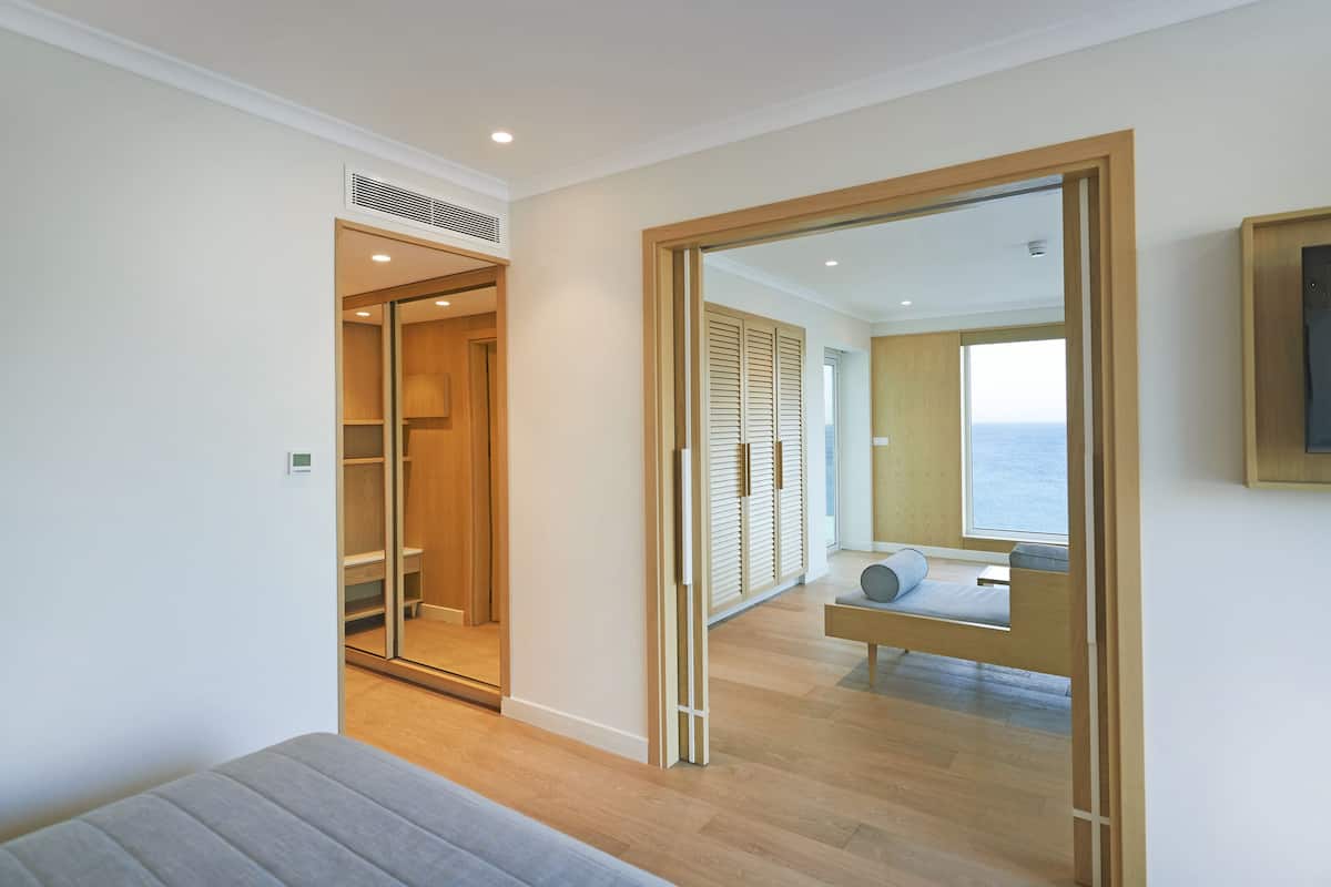 Une chambre moderne avec un plancher en bois, un lit, une armoire et une vue sur la mer par une grande fenêtre.