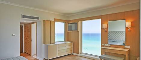 Un dormitorio moderno con un ventanal grande, una cama, un aparador de madera, una tocador con espejo y un banco.