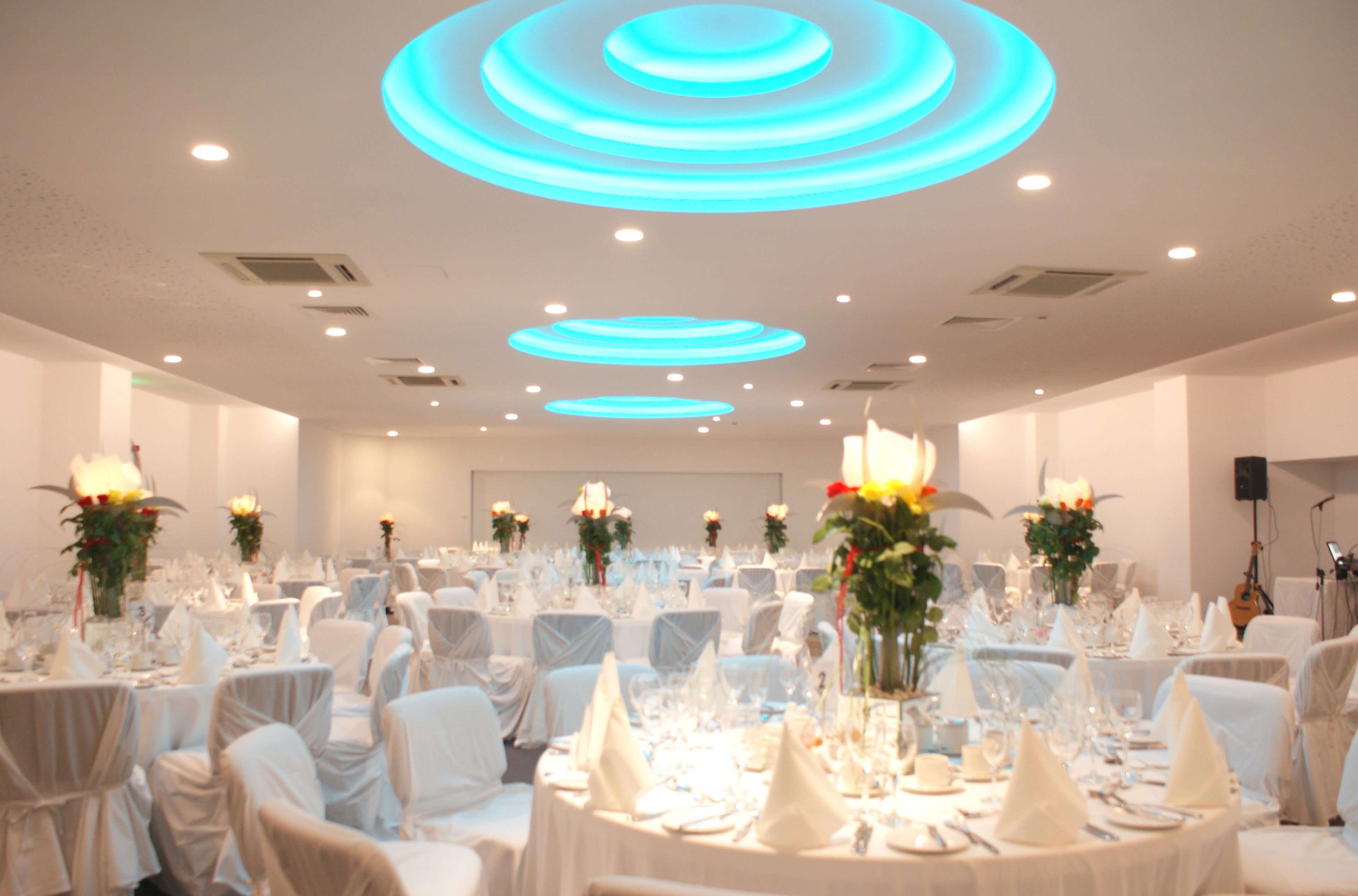 Een feestzaal met ronde tafels gedekt voor een formeel evenement, met witte tafelkleden en bloemstukken als decoratie.