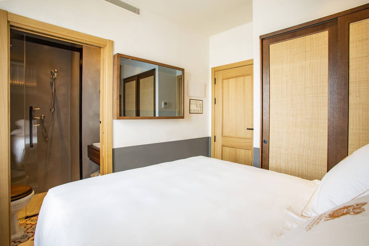 Ein Hotelzimmer mit einem Bett, einem Holzschrank, einem Badezimmer mit Dusche und einem Spiegel an der Wand.