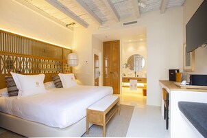 A modern hotel room with a large bed, a wooden headboard, a bedside table, a desk, and a mirror.