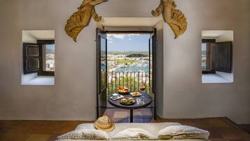 Una stanza con un balcone, un tavolo imbandito di cibo e bevande, e due finestre con tende.