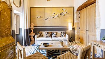 A room with a sofa set, a wooden table, wicker chairs, a decorative wall piece, and a stone wall.