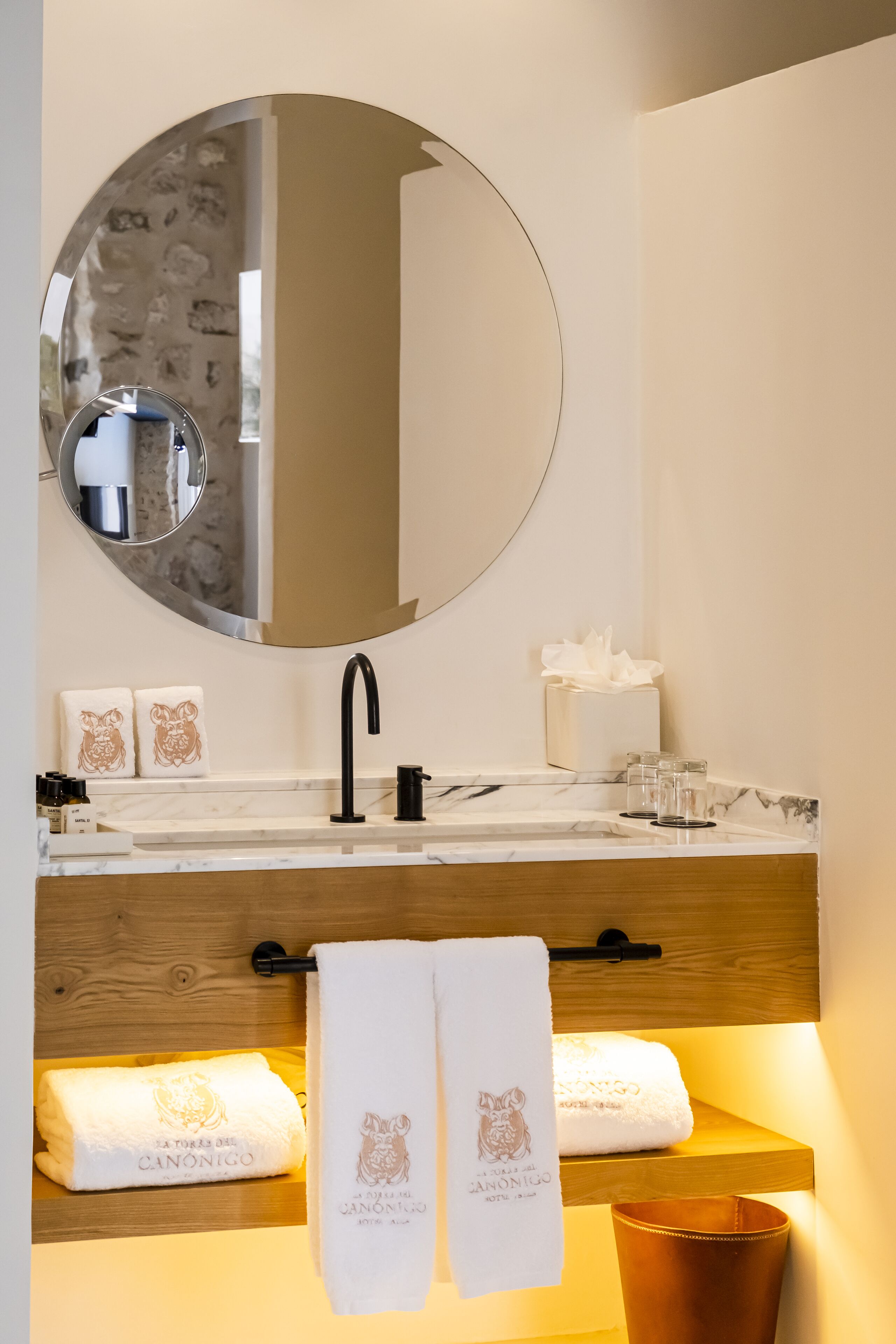 Een moderne badkamer met een ronde spiegel, een zwarte kraan en twee handdoeken met een leeuw dessin.