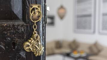 Primer plano de un llamador de latón con diseño decorativo, una cerradura y un aplique de pared al fondo.