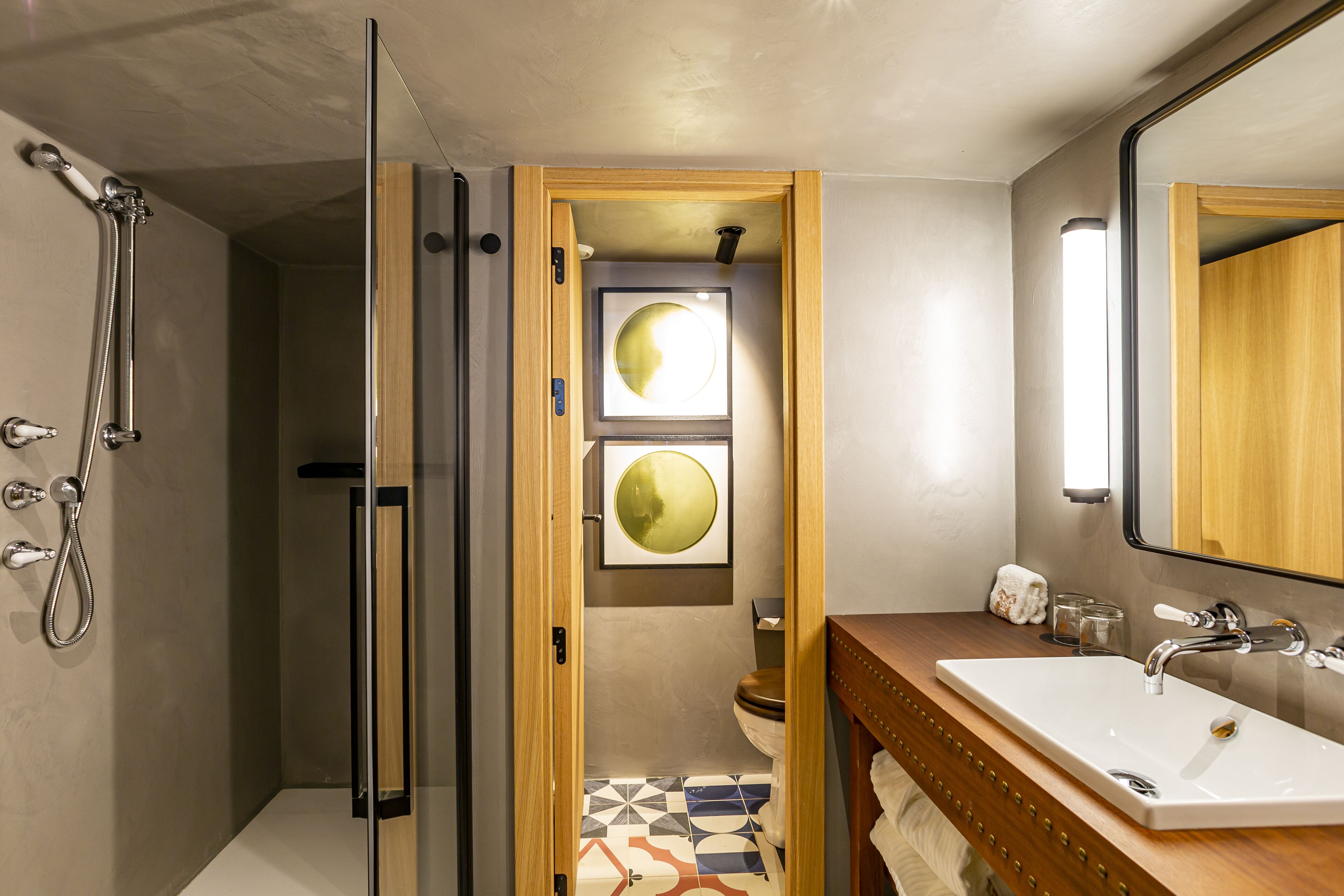 Un baño moderno con cabina de ducha de vidrio, un mueble de tocador de madera con lavamanos blanco y dos espejos redondos fijos en la pared.