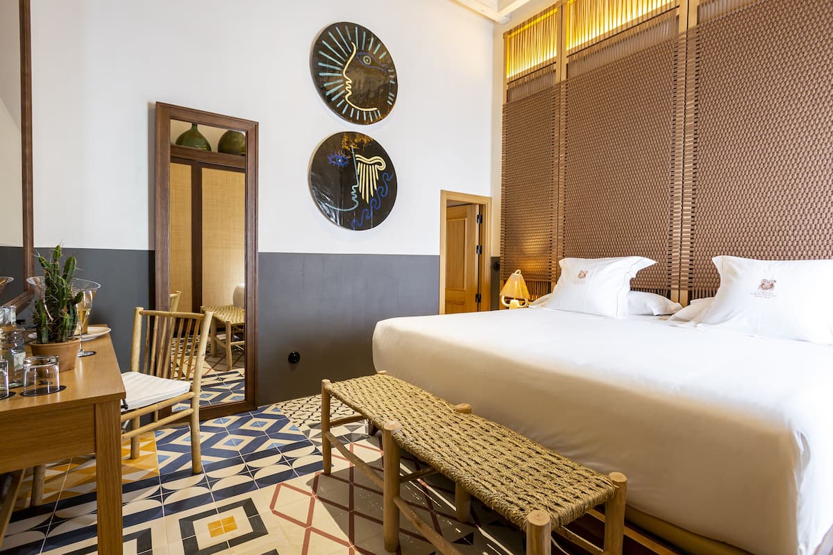 Ein Hotelzimmer mit Bett, einer Bank, einem Esstisch mit Stühlen und Wanddekoration.