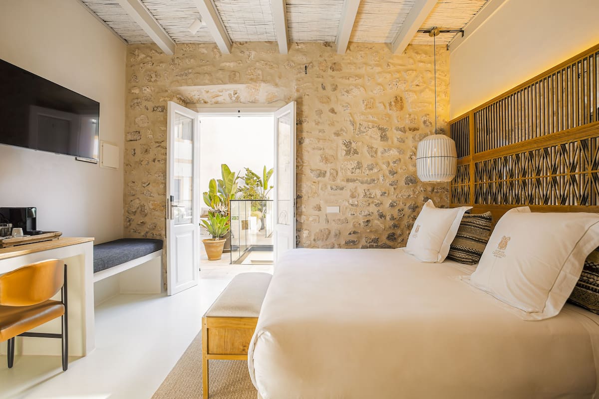 Ein Schlafzimmer mit Steinsandsteinwand, einem Bett mit weißer Bettwäsche, einem Holz-Kopfteil, einem Fernseher, einem Schreibtisch mit Stuhl und einer Topfpflanze.