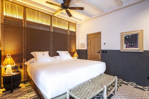 Habitación de hotel con una cama grande, ventilador de techo, puerta de madera y un cuadro colgado en la pared.