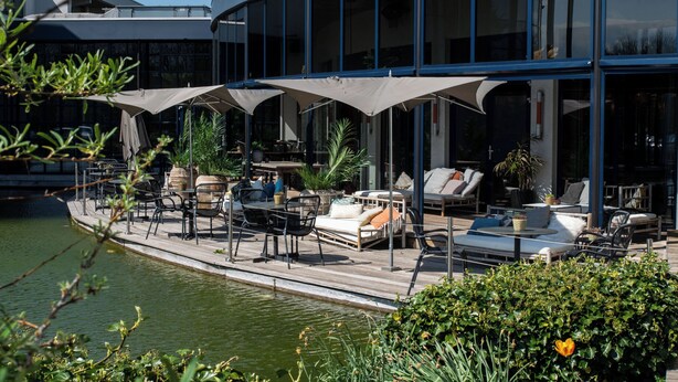 Un patio frente al agua con mobiliario exterior, incluyendo sillones y mesas, además de una piscina.