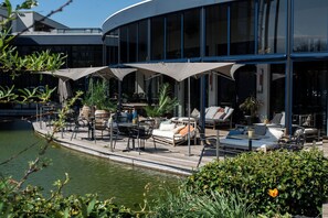 A waterfront patio with outdoor seating, including lounge chairs and tables, and a pool. - Van der Valk Hotel Sassenheim - Leiden (Sassenheim)