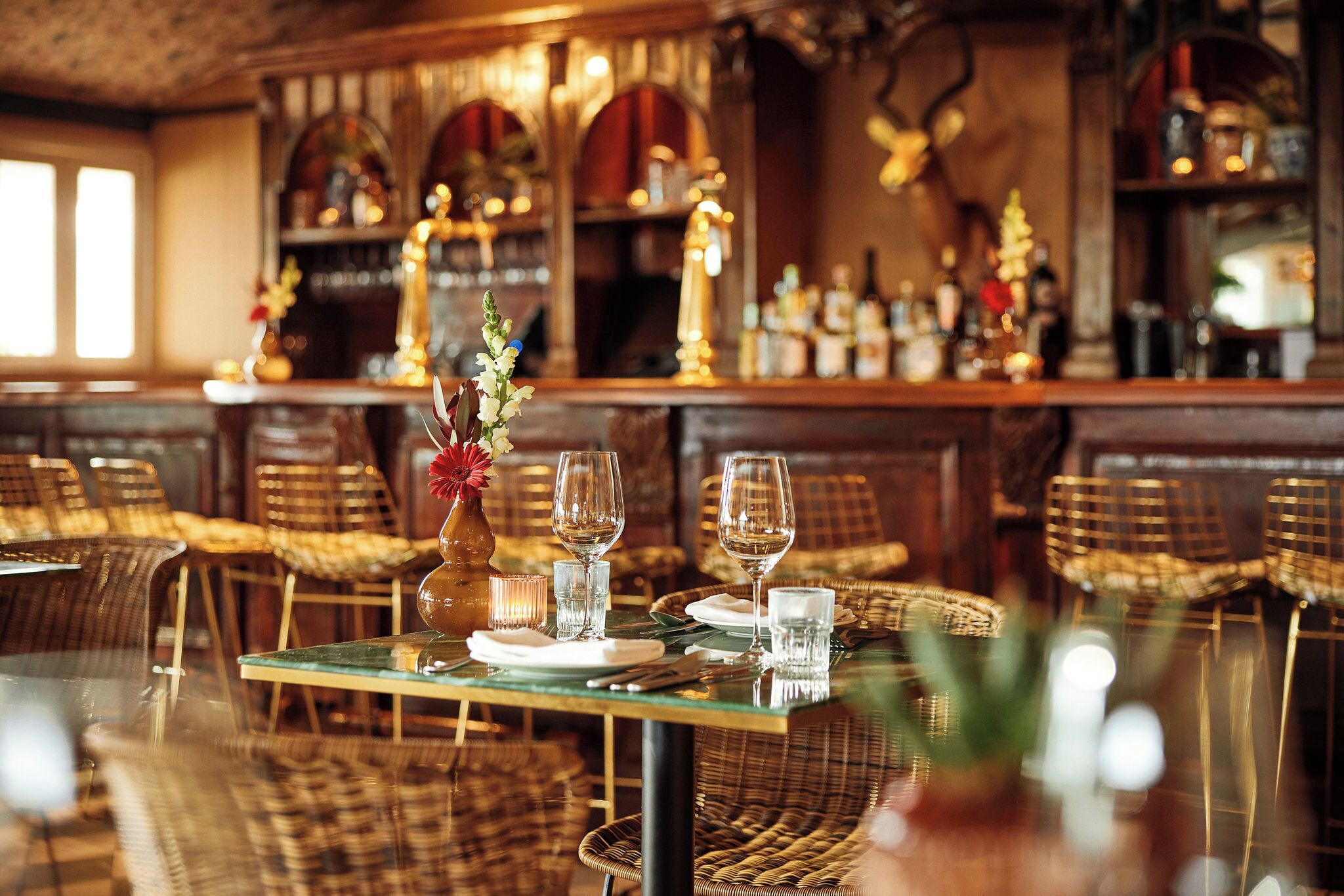 A restaurant with wicker furniture, a bar area with bottles, and a decorative vase with flowers.