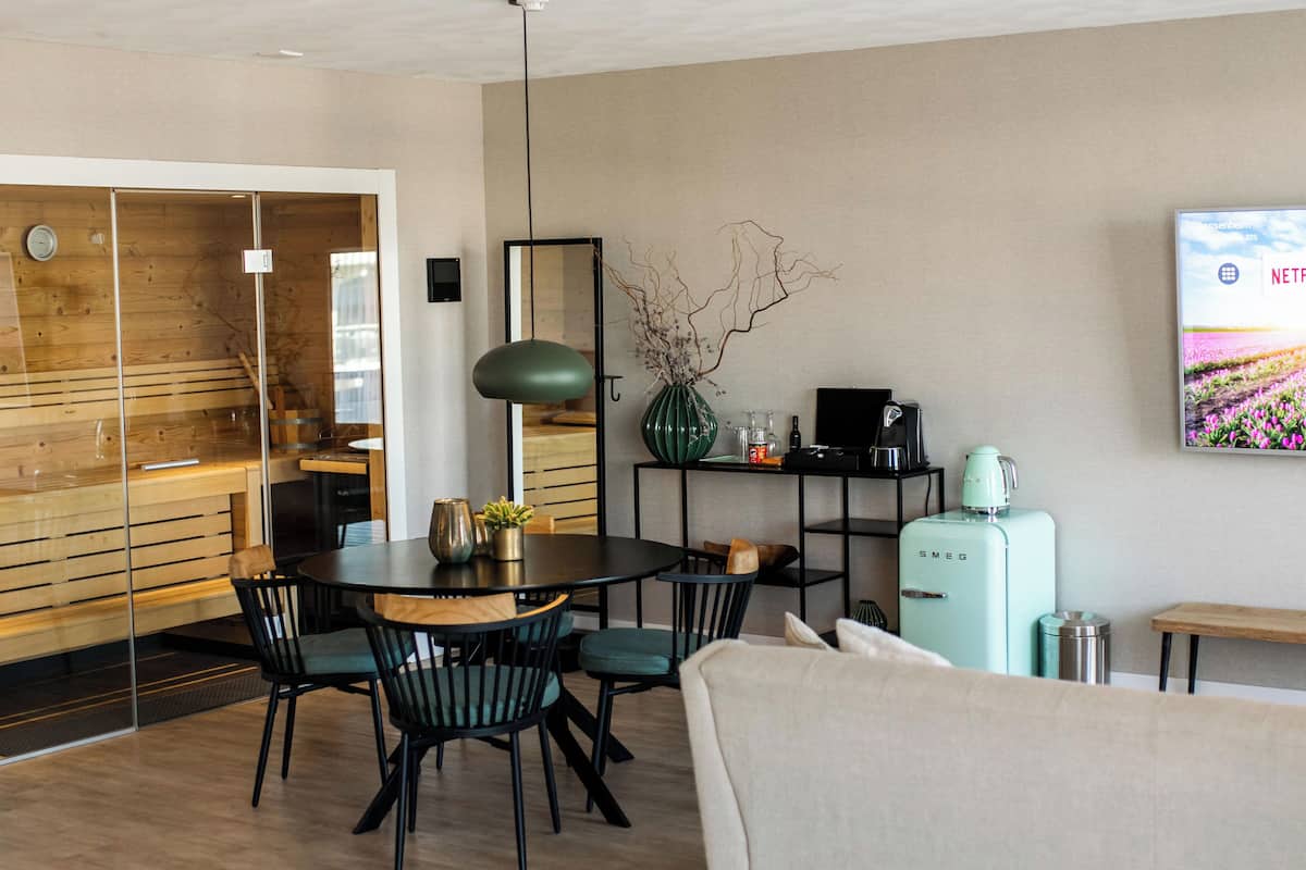 Una sala moderna con comedor, un refrigerador de estilo vintage y un televisor de pared que muestra una escena natural.