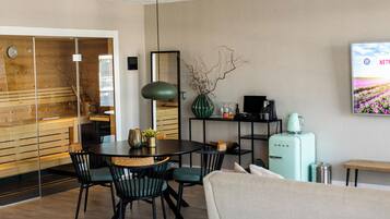 Un salon moderne comprenant un coin repas, un réfrigérateur de style vintage et un téléviseur fixé au mur qui diffuse une scène de la nature.
