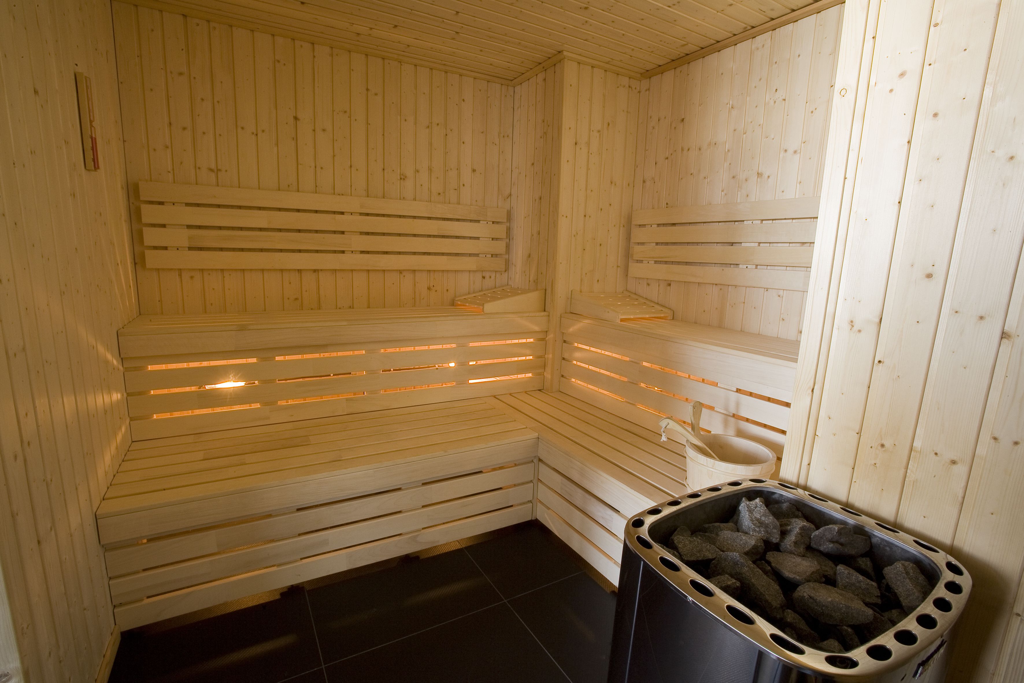 A sauna with wooden benches and a trash bin filled with rocks.