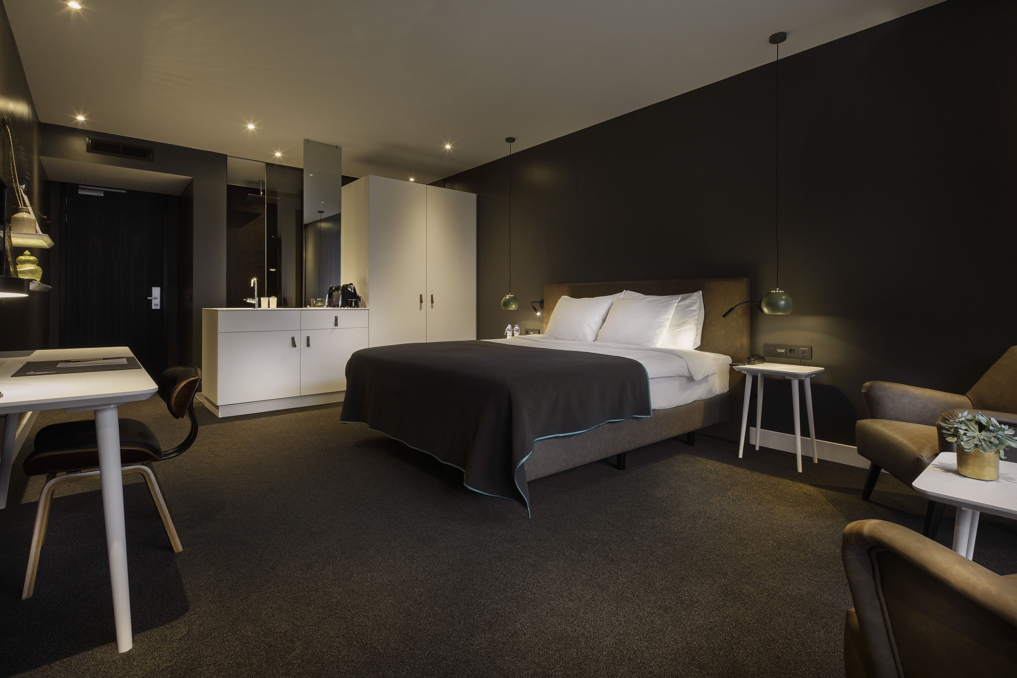 A modern hotel room with a large bed, a desk, a chair, and a small table.