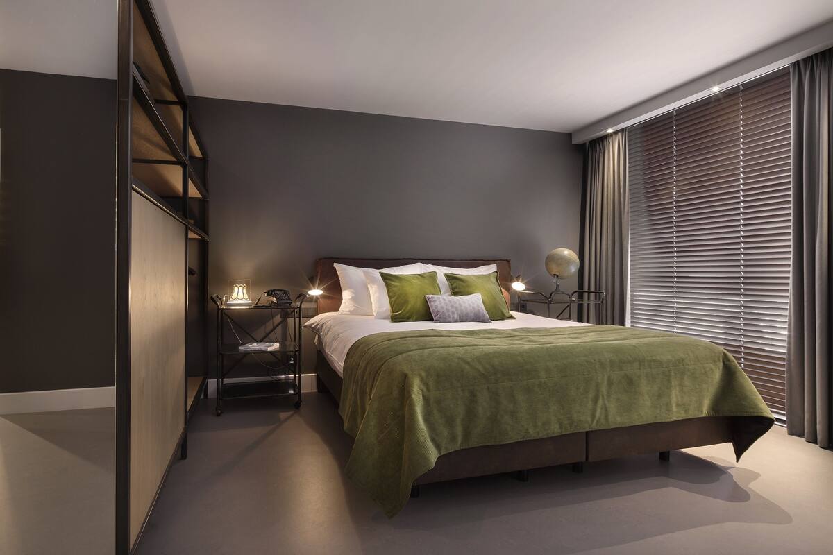 Un dormitorio moderno con una cama grande, un tocador con iluminación y vistas a través de ventanales de pared a techo.