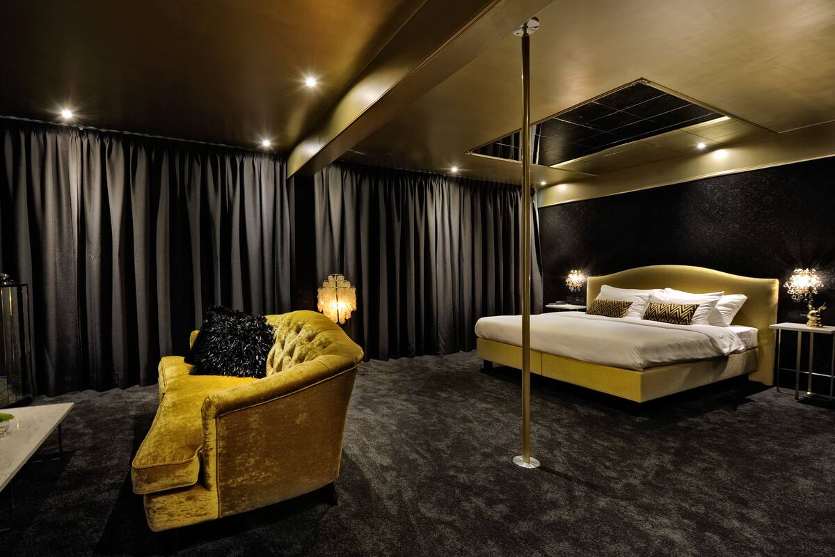 Una habitación de hotel con una cama grande, un sillón dorado y una lámpara de pie.