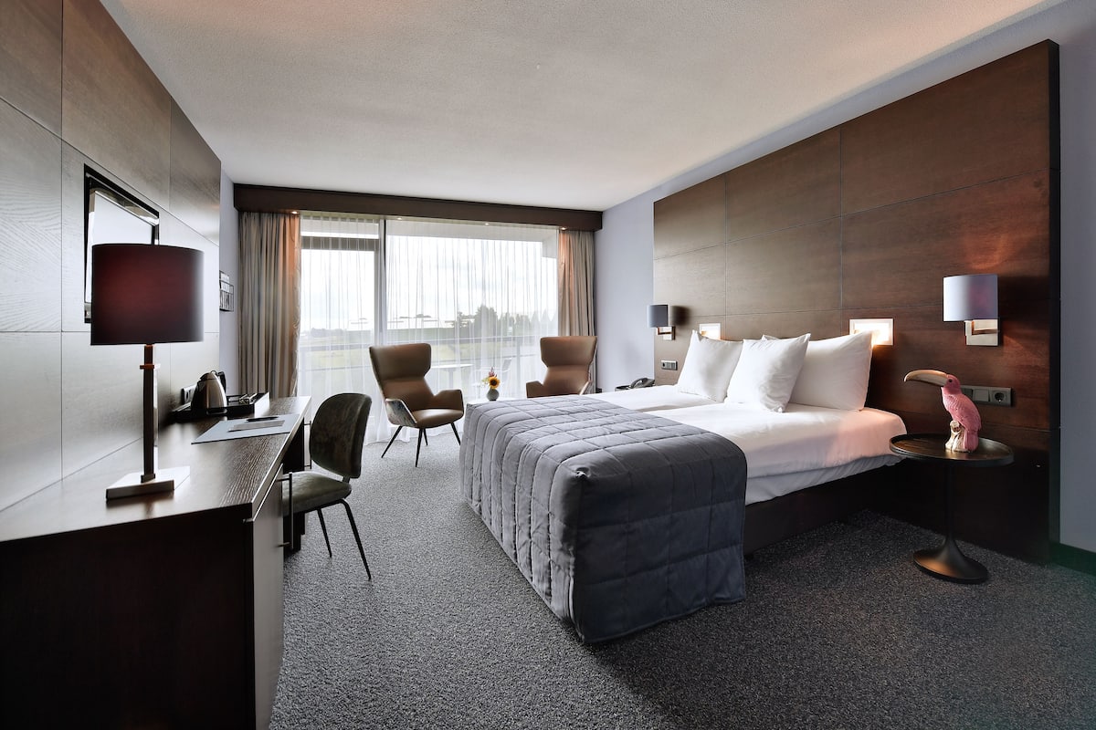 Una habitación de hotel con una cama, escritorio, sillas y una mesita de noche con lámpara.