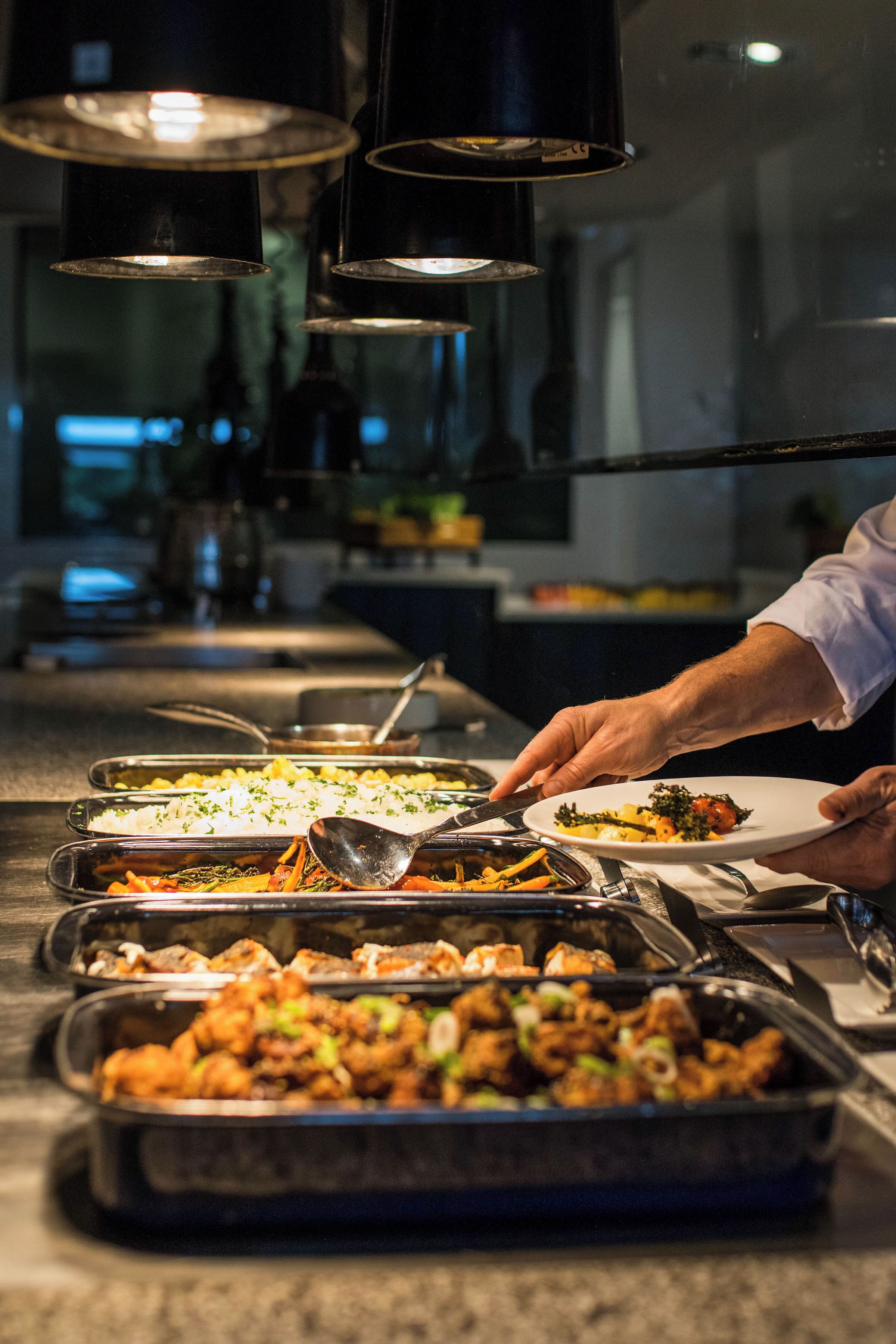 A buffet setup with various dishes and a person serving food.