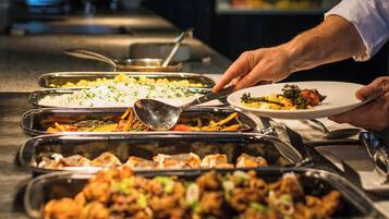 A buffet setup with various dishes and a person serving food.