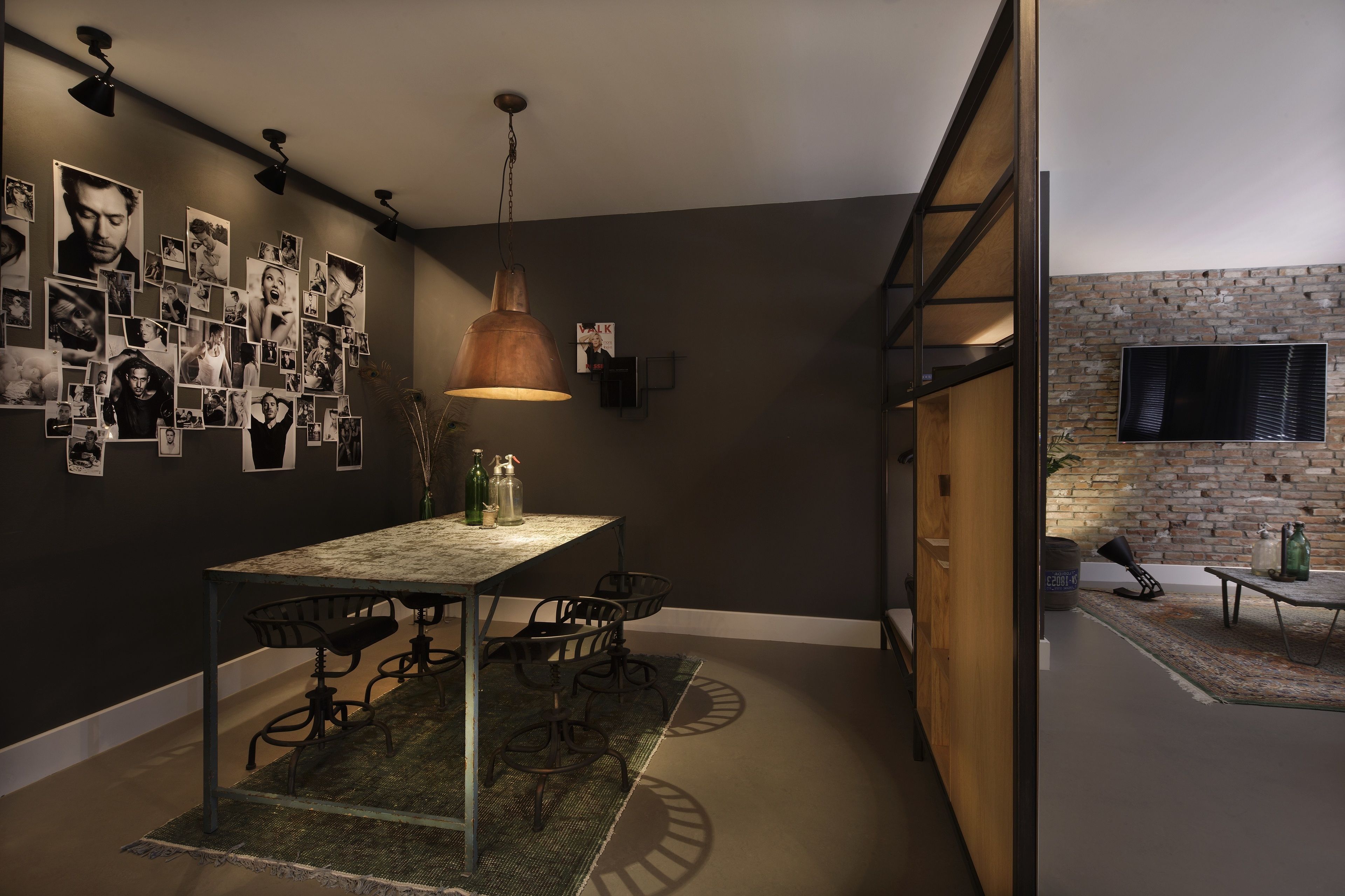 A modern dining area with a table and chairs, a hanging pendant light, and a wall adorned with photographs.