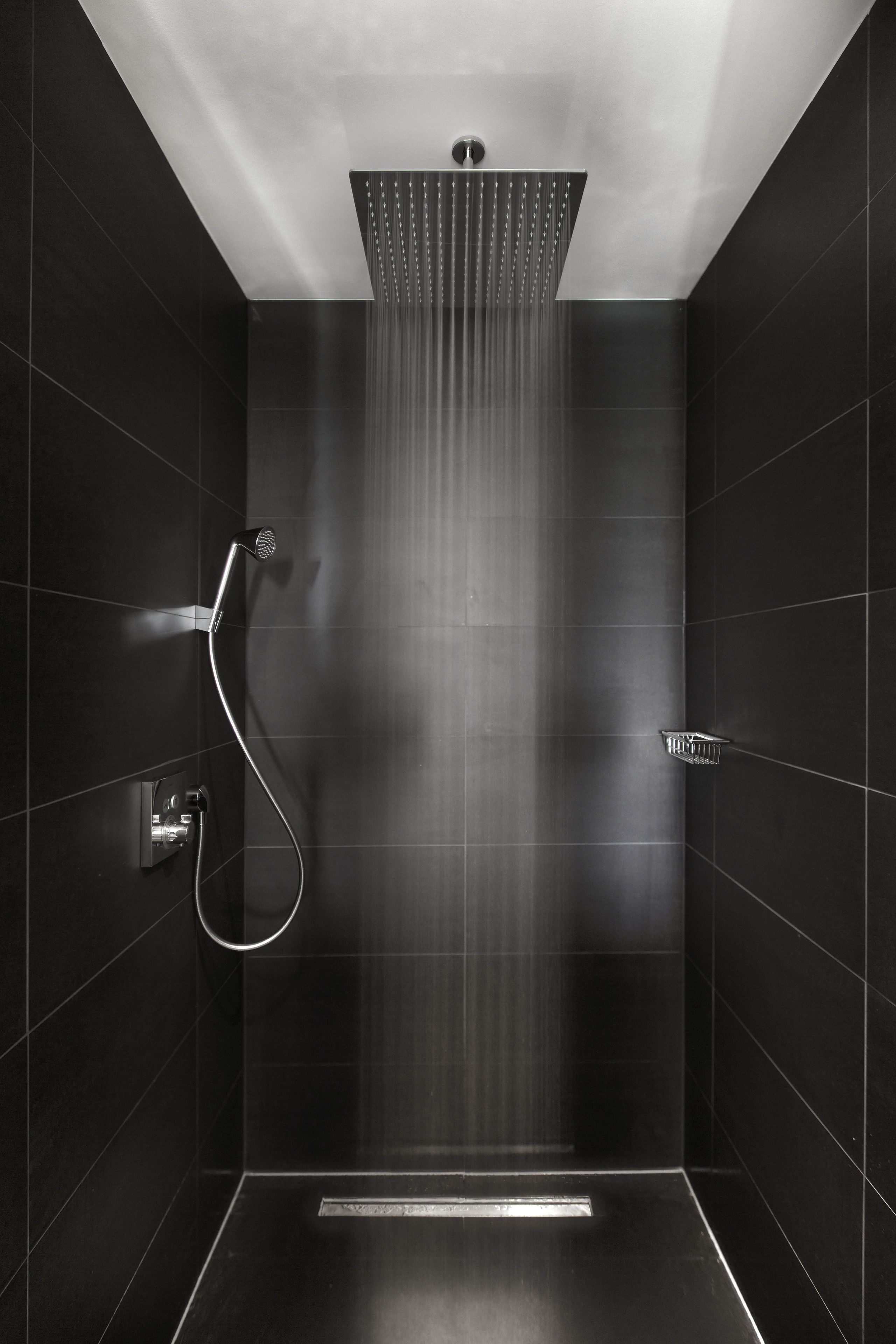 A modern shower with a vertical rain showerhead, a handheld showerhead, and a control panel.