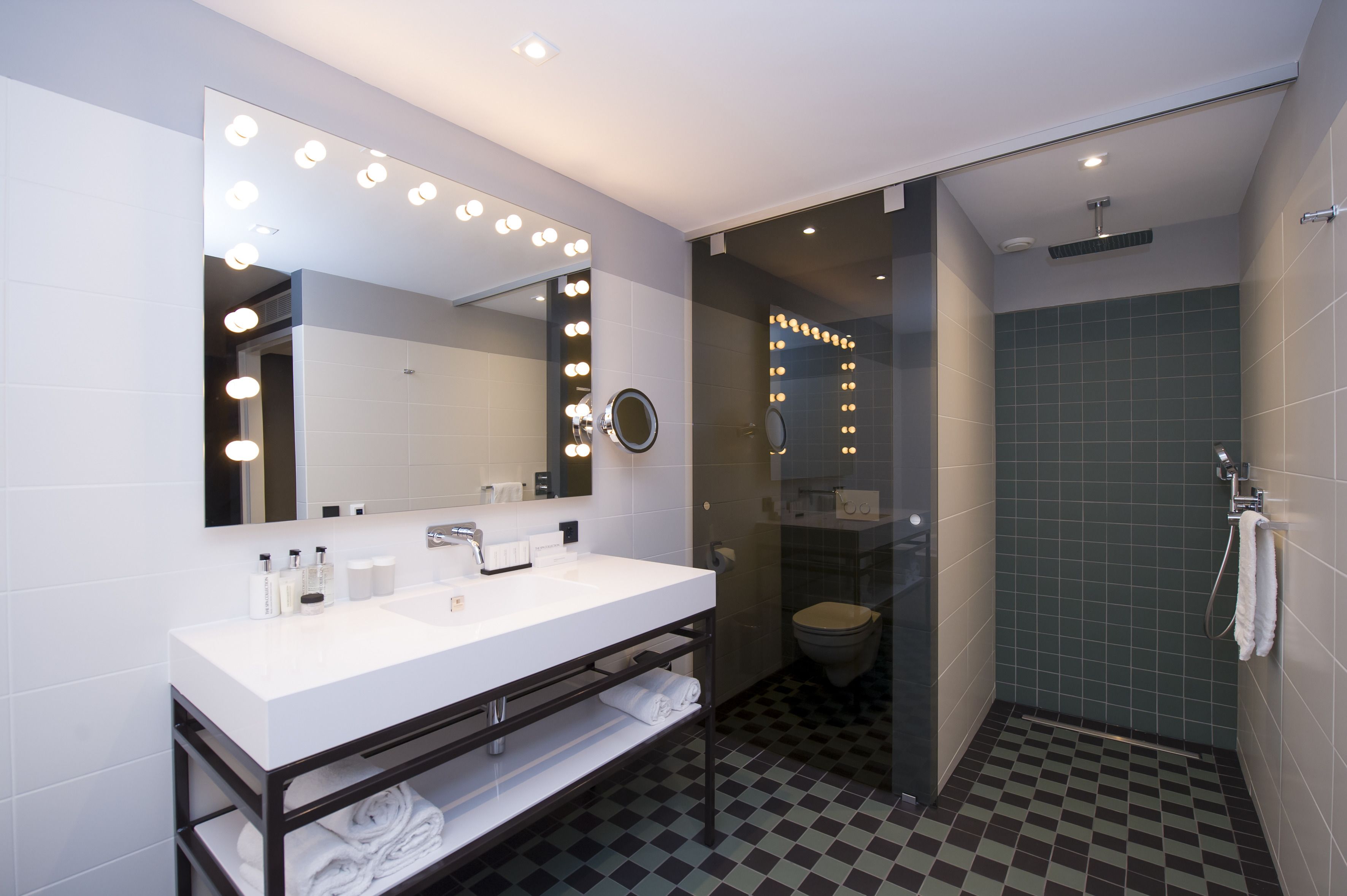 A modern bathroom with a white sink, large mirror with lights, and a shower area.