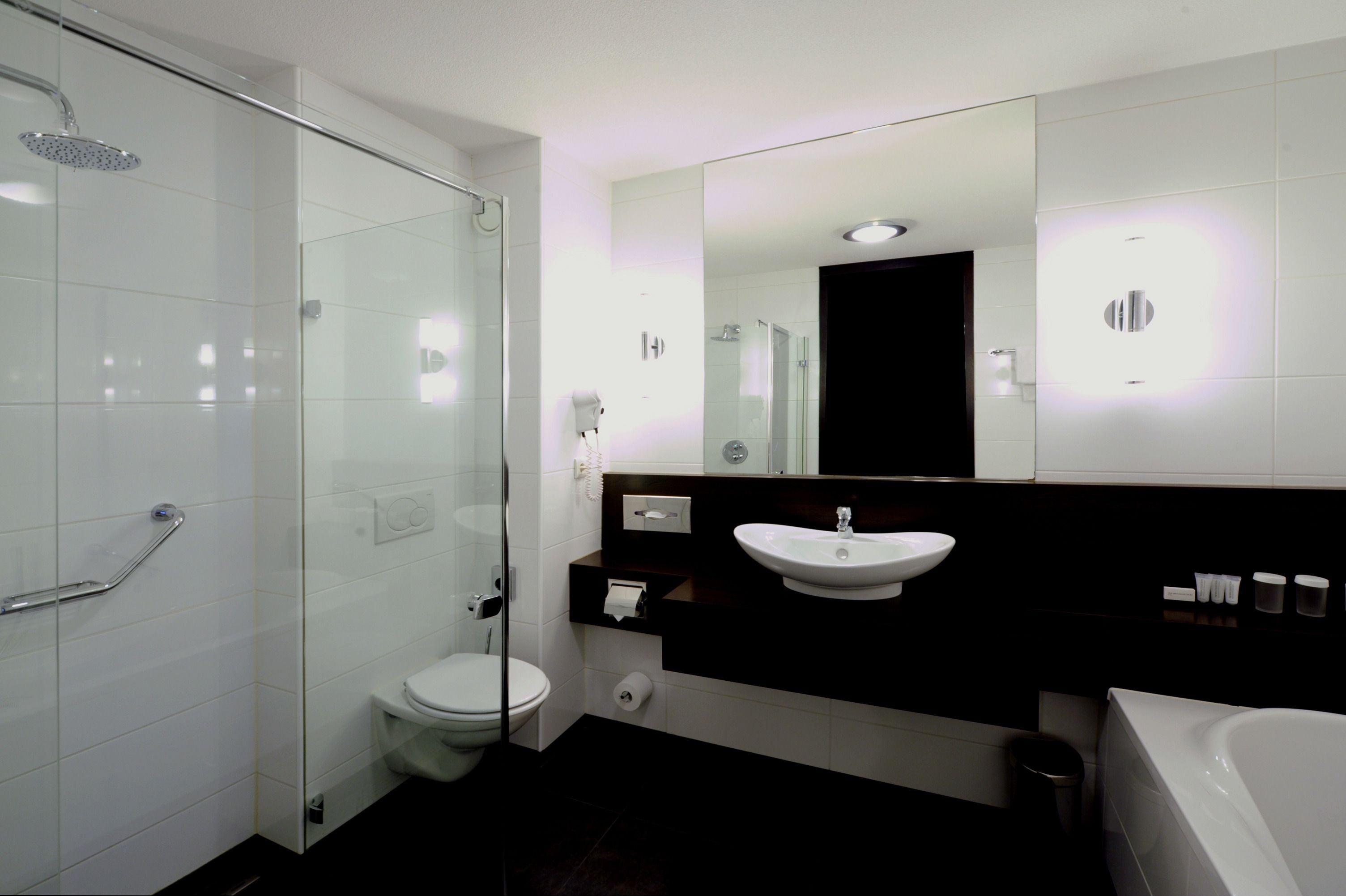 A modern bathroom with a glass shower enclosure, a white toilet, a sink with a mirror above, and a bathtub.