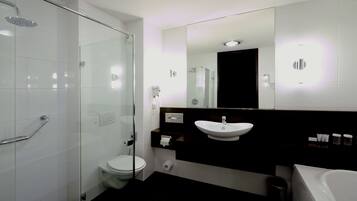 Une salle de bain moderne avec une douche à parois de verre, des toilettes blanches, un lavabo avec un miroir au-dessus et une baignoire.