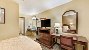 Una habitación de hotel con cama, escritorio, cómoda, televisor y espejo.