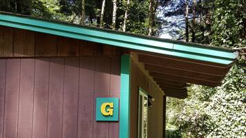 A wooden cabin with a green roof, labeled 'G', surrounded by dense greenery and trees.